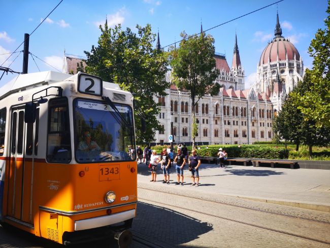 Yellow Tram in front of the Budapest Parliament building - Trams in Budapest are Cheap and Scenic too - Cheap Things to do in Budapest
