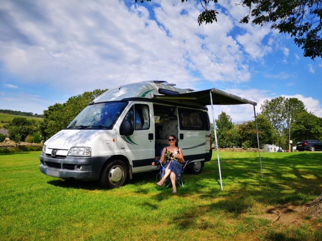Claire sat outside her Motorhome in a field - Enjoying the Solo Van Life 