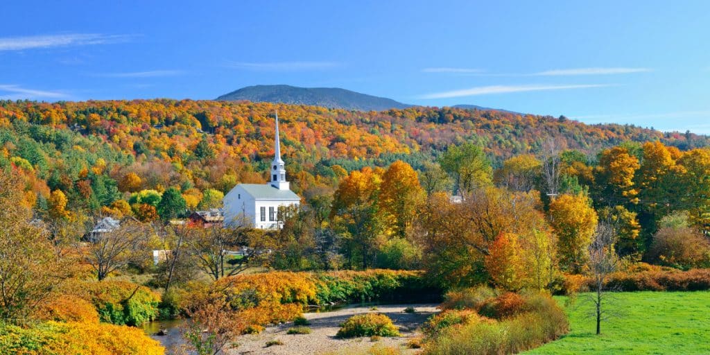 White church surrounded by trees in fall - The Best Places for Fall Foliage in the USA - Fall in New England
