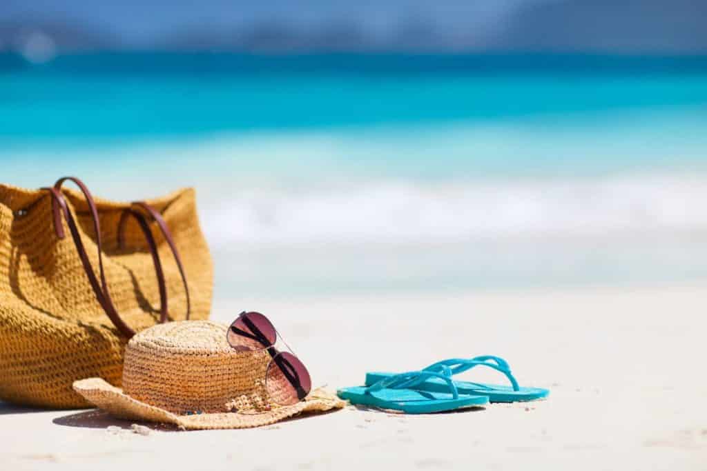 Flip Flops, hat and bag on the beach -Beach Packing List - What to Pack for the Beach