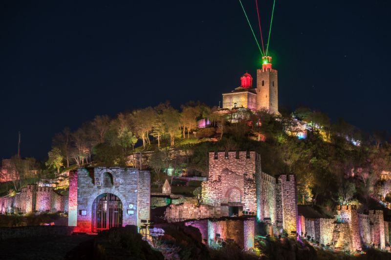 Tsarevets Fortress in Veliko Tarnovo Bulgaria at night, with a right green laser light shining up from a tower at the top of the hill
