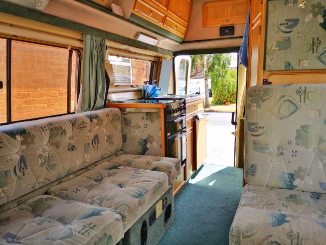 The Living Area in my Campervan - Sofa on one side of the van with the kitchen behind next to the backdoor. On the right is another seat then cupboards and toilet and a narrow walkway between them