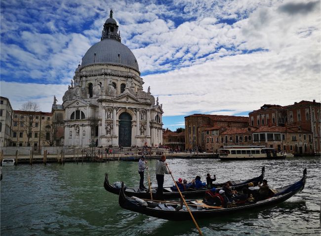 How to Visit Venice Sustainably - two gondolas on a Venice canal pass in front of a domed church
