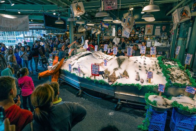 Fishermen throw their fish while visitors look on at Pike Place Fish Market - Free Things to do in Seattle
