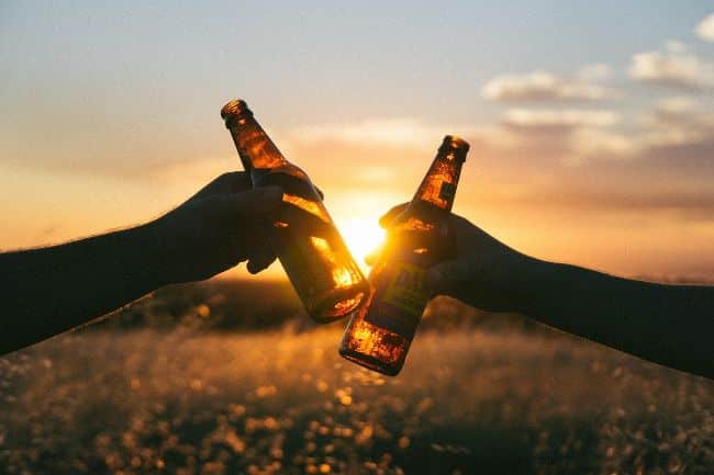 Hands Holding Beer Bottles to Cheers as the sun goes down behind - Beers with New Friends Is Always More Appealing than Work!