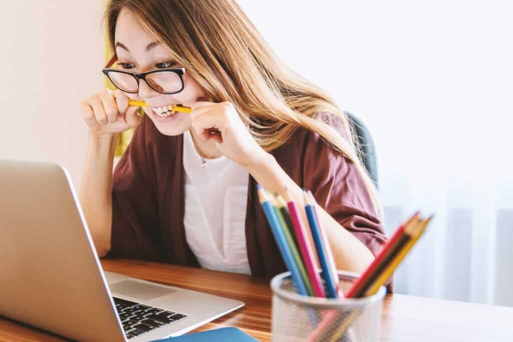 Woman sta at a laptop looking frustated and biting a pencil - How to Be a Digital Nomad with No Skills