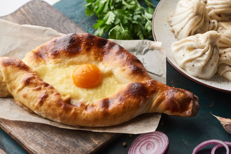 Georgian food - Khachapuri boat shaped bread filled with chees and egg with a plate of dumplings