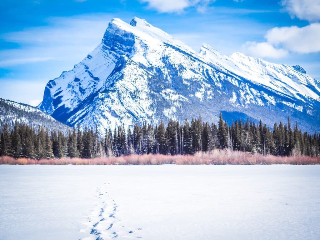 Frozen Lake in Banff with footsteps in the snow leading towards a striking mountain on the horizon- The Best Things to do in Banff in Winter