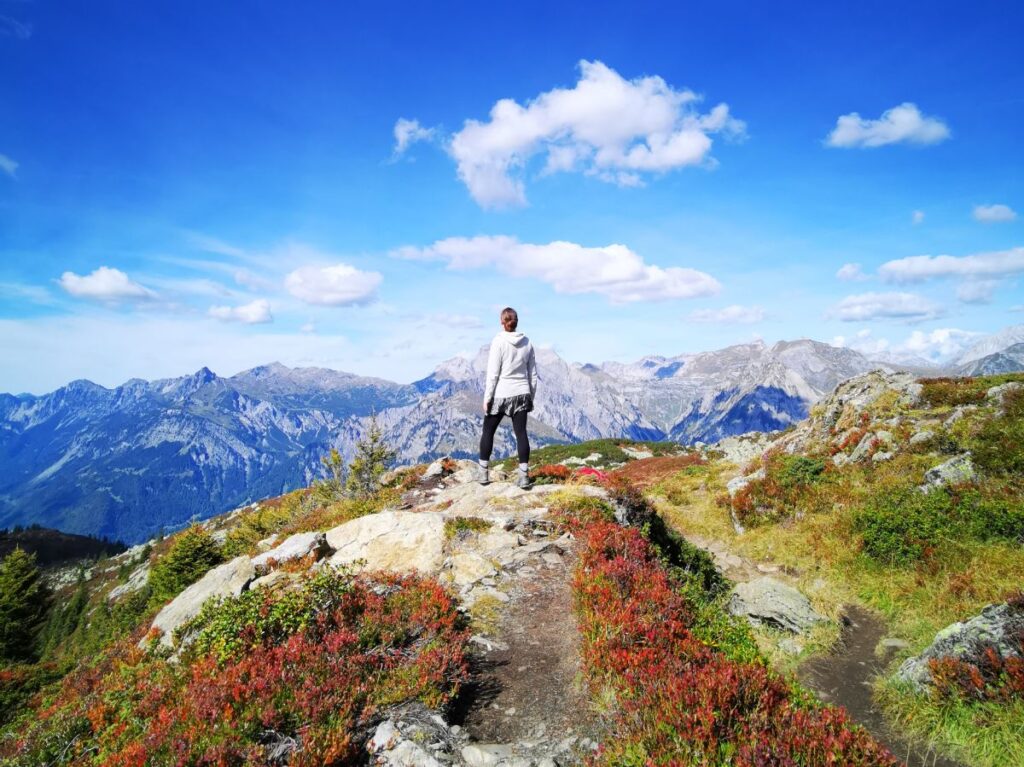 Hiking for Beginners - Woman with her back to the camera looking out at mountains from the peak of a hiking trail