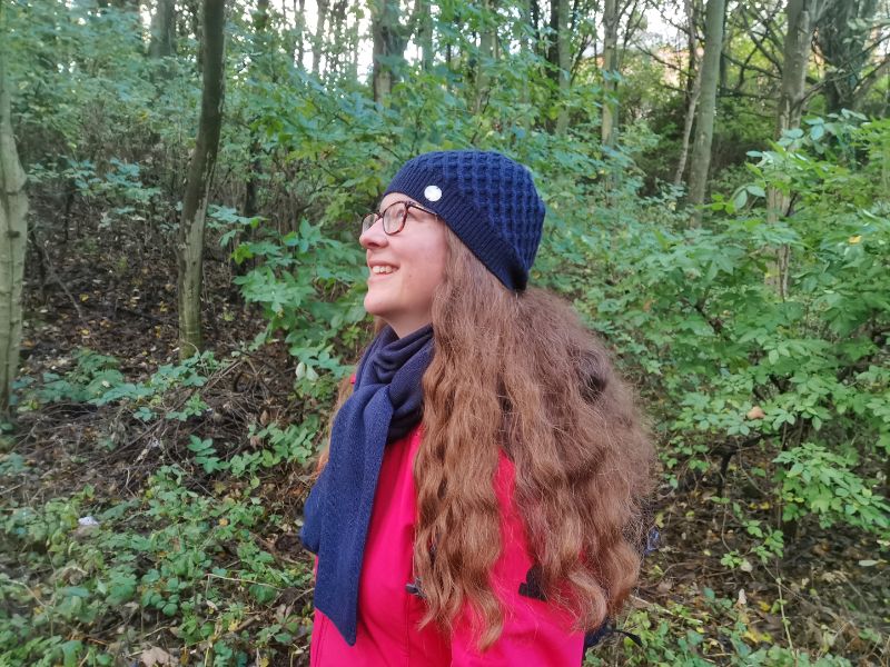Hiking Gifts - Claire in the forest wearing a red jacket and a dark blueWoolly Hat and Scarf