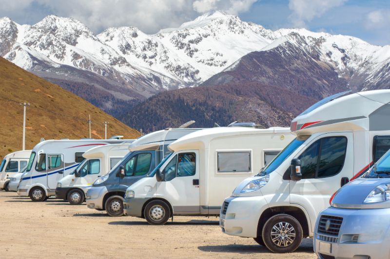 A row of motorhomes in a campground with snowy mountains in the background - Campervans and Motorhomes Come in All Shapes and Sizes