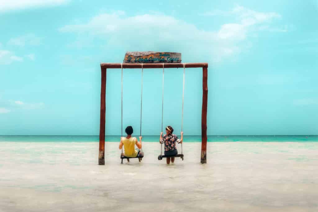 Couple sitting on swings on the beach at Holbox with turquoise blue water all around