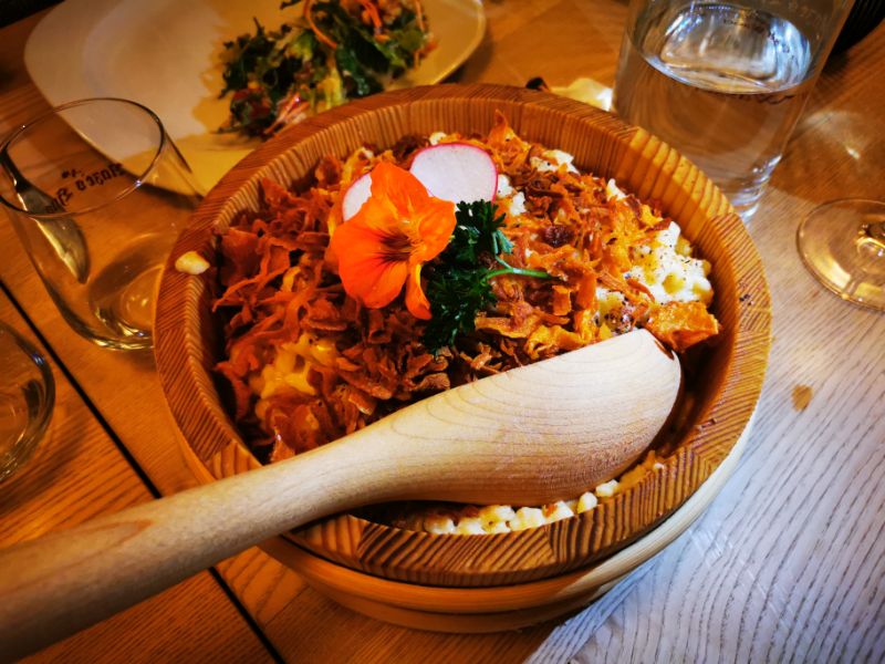 Cheesy Kasspatzle decorated with fried onion pieces and an orange flower in a traditional wooden dish