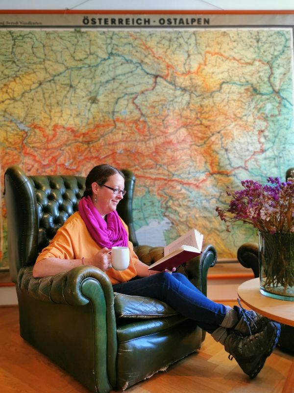 Me Relaxing in Vorarlberg on an armchair reading a book in front of a map of Austria