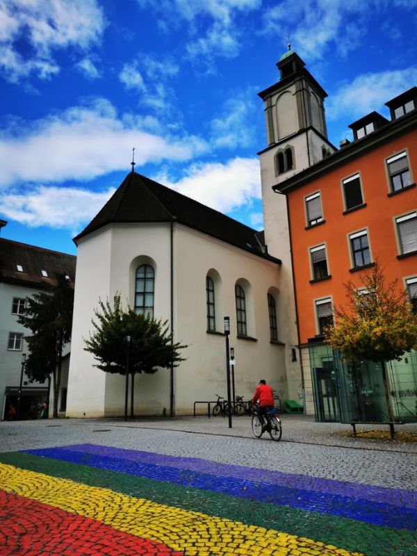 The Colourful Streets of Feldkirch - A Rainbow painted on the floor of a square in Feldkirch, with a church in the background