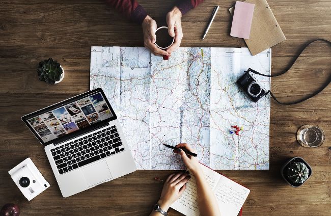 Overlay of a map with two people's hands planning with a laptop and notebook