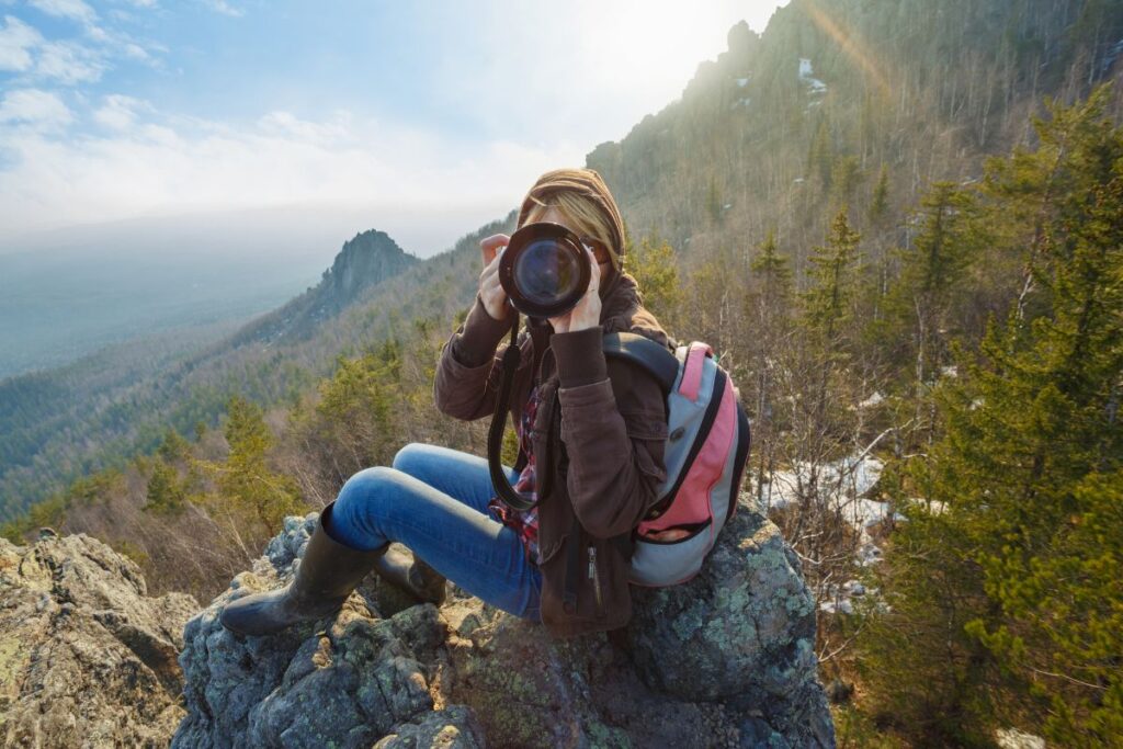 The Best Backpacking Camera for Backpackers and Hikers - Woman pointing a camera at the photographer, at the top of a wooded hillside on a hike