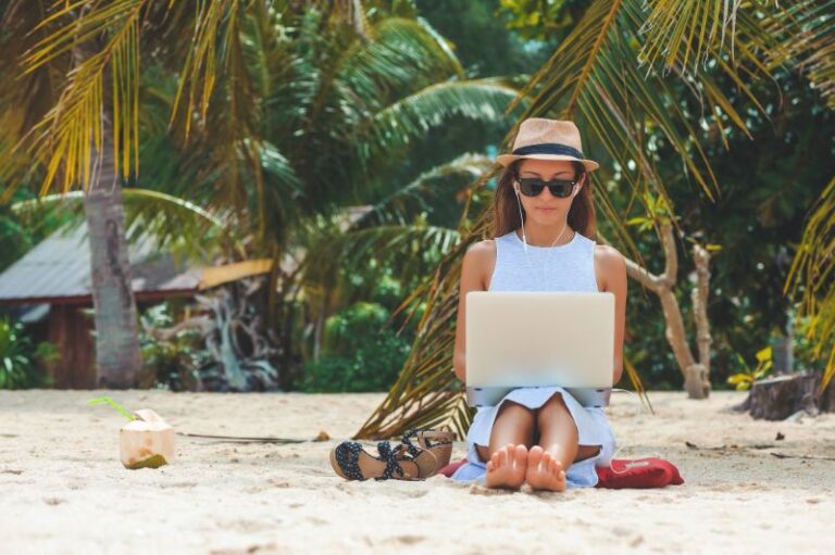 Woman working abroad using a laptop while sitting on a beach - work exchanges and finding work abroad