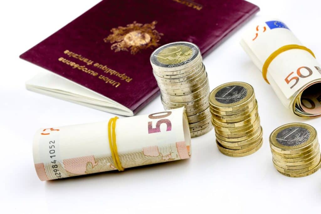 Passport with piles of coins and rolls of cash - How to Earn Money While Travelling - Tips for earning money on the road