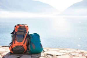 Two backpacks on the ground with a beautiful lake behind them - What to Pack in A Backpack - Backpack Essentials for Travel