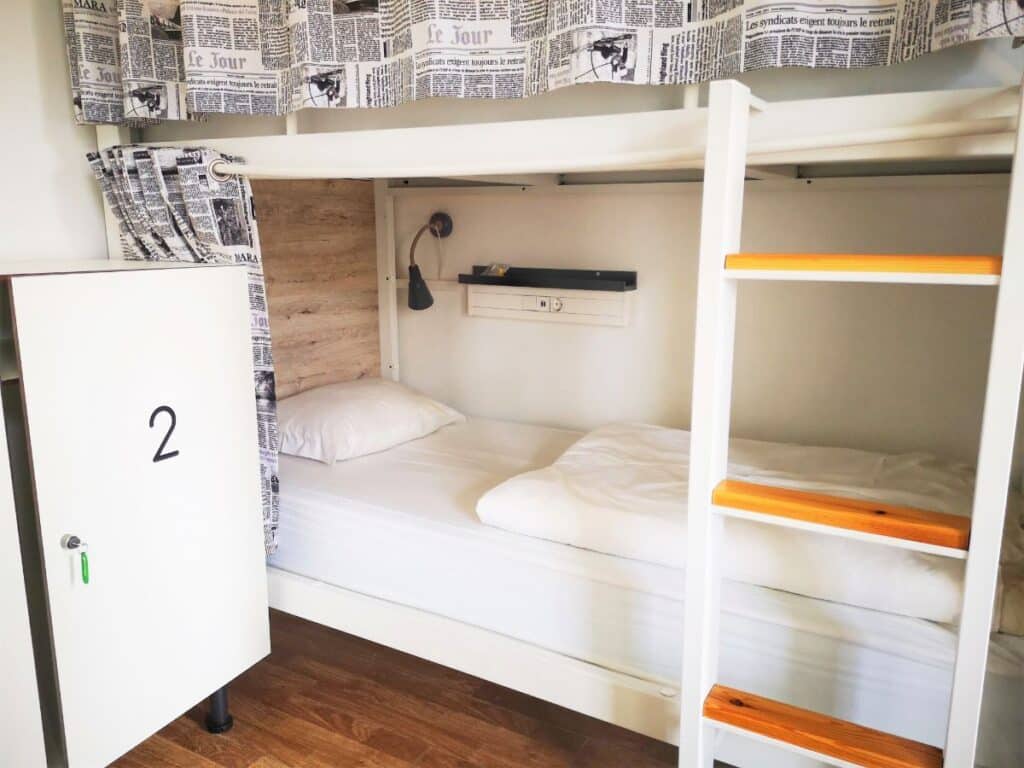 Clean Hostel Bunk Bed with white sheets and a white locker door - Should you Work for Accommodation?