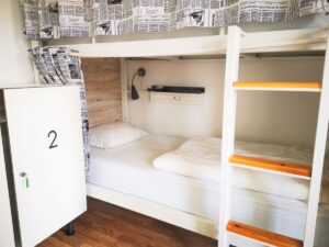 Clean Hostel Bunk Bed with white sheets and a white locker door - Should you Work for Accommodation?