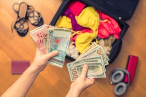 How to Hide Money While Travelling - Woman holding handfuls of cash above her open suitcase