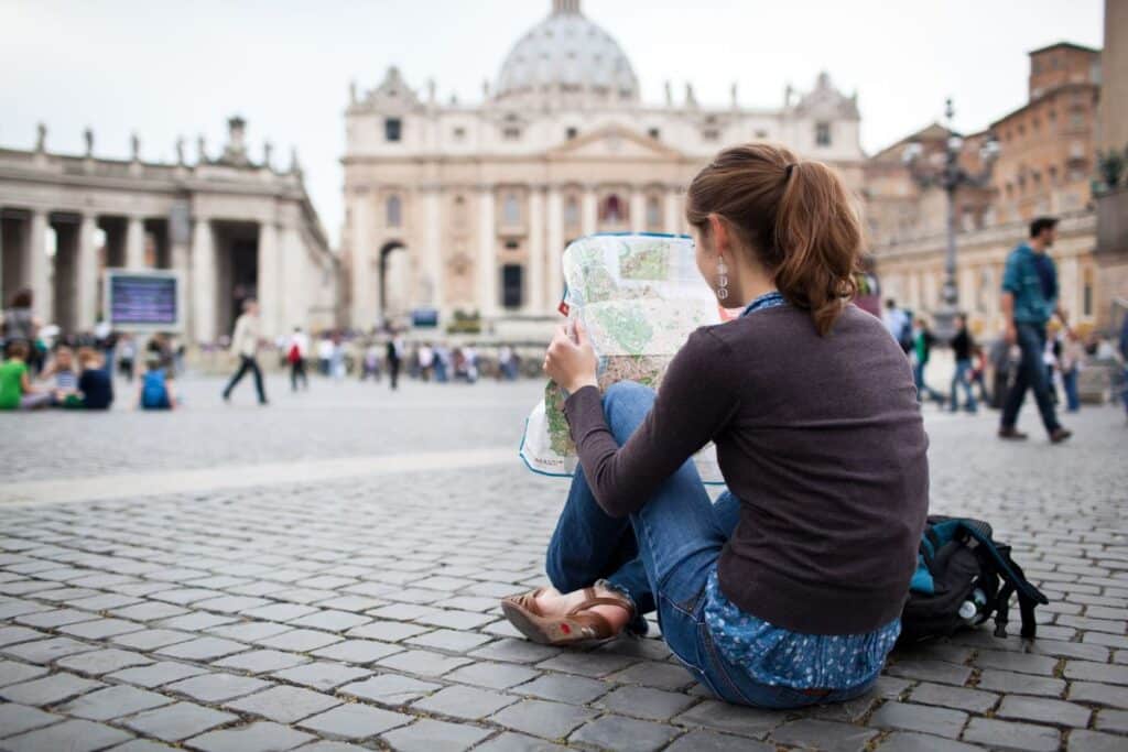 Female backpacker sitting down in a square reading a map