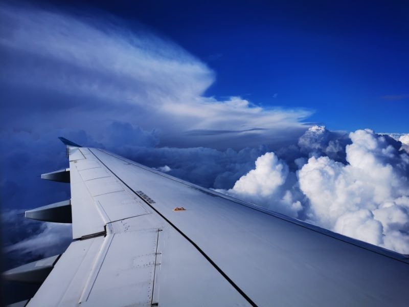 Airplane wing in flight with blue sky and clouds around - Long Haul Flight Tips