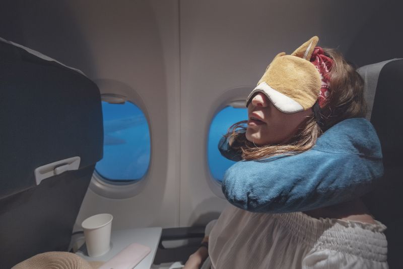 Women sleeping on a plane wearing an eye-mask and using a travel pillow