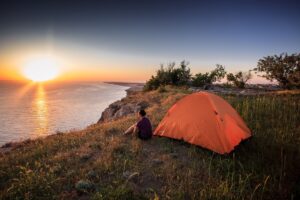 Orange tent pitched outdoors with a beautiful view of the sunset - Camping Tips - Sustainable Camping Gear
