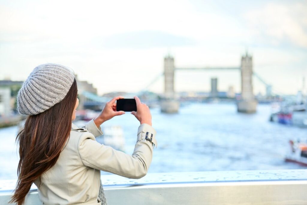 A woman taking a photo of Tower Bridge - What to Wear in London in Winter